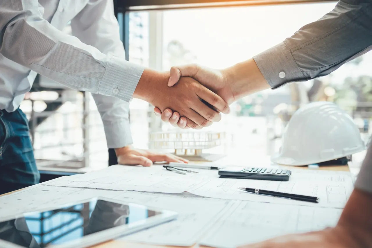 Handschlag über Bauplänen im Büro